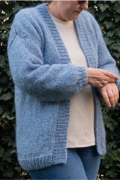 a woman wearing a blue cardigan standing in front of bushes