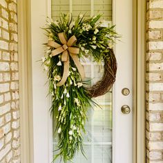 a wreath on the front door of a house with white flowers and greenery hanging from it