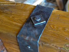 a close up of a piece of metal on top of a wooden table with screws