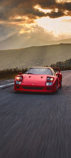 a red sports car driving down the road in front of a mountain range at sunset