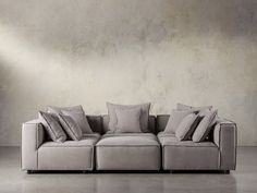 a couch with many pillows on it in front of a concrete wall and flooring