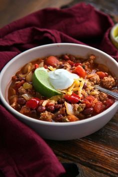 a white bowl filled with chili, beans and avocado on top of a wooden table