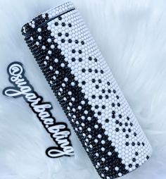 the black and white beaded case is next to a coca - cola can on a furry surface