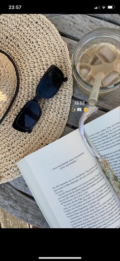 an open book sitting on top of a wooden table next to sunglasses and a straw hat