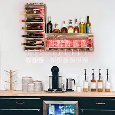 there are many bottles and glasses on the shelf above the wine glass rack in this kitchen