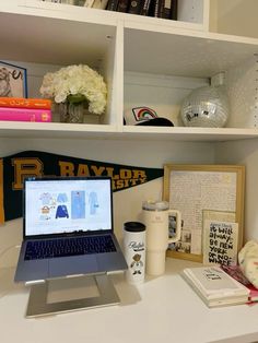 an open laptop computer sitting on top of a white desk next to books and other items