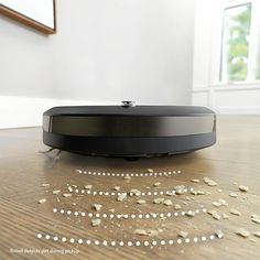 a roomba that is on the floor with some white beads scattered around it and there are two windows in the background