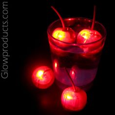 some red apples are in a glass filled with water and lit by candlelightes