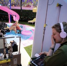 a woman with headphones sitting in front of a camera and another person on a laptop