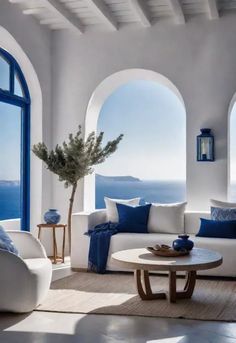 a living room filled with white furniture and blue accents on the windows overlooking the ocean