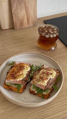 a plate with two sandwiches on it next to a glass of tea and a wooden cutting board