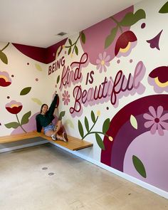 a person sitting on a bench in front of a wall with flowers and the words being kind is beautiful