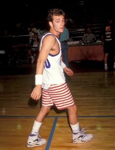 a man standing on top of a basketball court wearing red and white striped shorts with his hands in his pockets