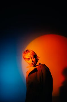 a woman standing in front of an orange and blue background with her head turned to the side