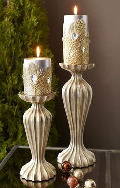 two white candles sitting on top of a table next to christmas ornaments and pine cones