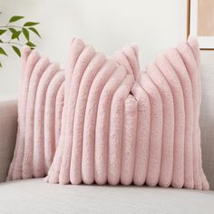 two pink pillows sitting on top of a couch next to a potted green plant