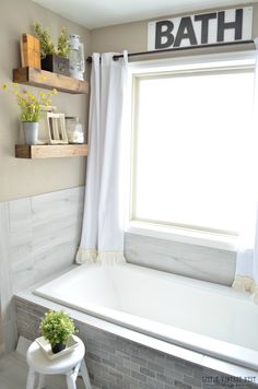 a bath tub sitting under a window next to a white chair and shelf filled with flowers