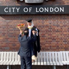 two men in graduation gowns standing next to a bench