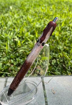 a pen sitting on top of a glass stand in front of some green grass and bushes