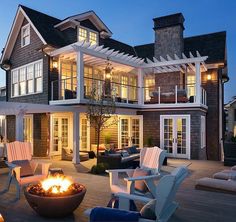 an outdoor fire pit is lit up in front of a large house with deck and patio furniture