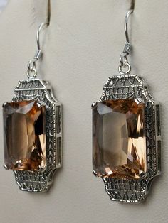 Simulated Peach Topaz EarringsLantern Design#E13 Inspired by the Art Deco period, these lovely antique reproduction earrings are sterling silver. Created from an antique brooch, each earring has a 9 carat simulated Peach Topaz surrounded by sterling silver filigree. The man-made gemstones are 15mm x 12mm each. The earrings are 1 3/4" long and 9/16" at their widest point. These lovely dangle earrings are marked 925 for sterling silver. These earrings are a wonderful blend of today and yesteryear. Elegant Silver Rectangular Earrings, Silver Rectangular Stone Earrings For Formal Occasions, Sterling Silver Rectangular Earrings For Wedding, Sterling Silver Wedding Earrings With Rectangular Shape, Elegant Antique Silver Rectangular Jewelry, Elegant Nickel-free Rectangular Jewelry, Vintage Jewelry With Rectangular Stone For Weddings, Elegant Rectangular Filigree Jewelry, Antique Jewelry With Rectangular Stone For Formal Occasions