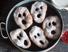 four sugary donuts with faces on them in a pan next to a cup and saucer