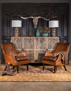 two brown leather chairs sitting in front of a wooden paneled wall with cow skulls on it