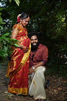 a man and woman sitting next to each other on the ground in front of trees