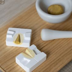 a wooden cutting board topped with two pieces of cheese next to a small white bowl