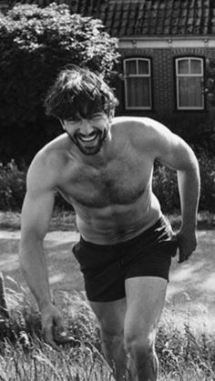 a shirtless man is running through the grass in front of a house and smiling