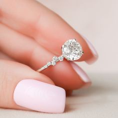 a woman's hand with a diamond ring on top of her finger and pink nail polish