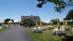 tables and umbrellas set up on the lawn for an outdoor wedding reception in front of a large white house