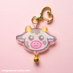 a cow shaped keychain hanging from a gold colored metal hook on a pink background