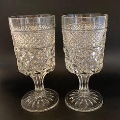 two clear glass goblets sitting side by side on a black surface with no one around them