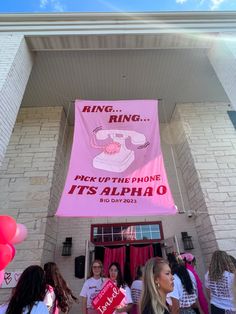 some people are standing in front of a building with a pink sign that says ring up the phone it's alphao