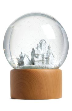 a snow globe with houses and trees inside on a wooden stand against a white background