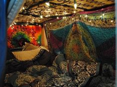 a bed covered in lots of blankets and pillows with lights strung from the ceiling above it