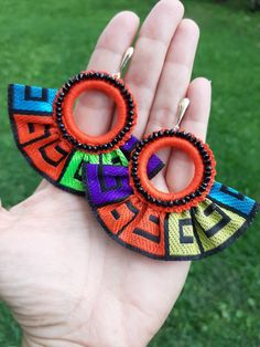 a hand holding two pairs of colorful earrings