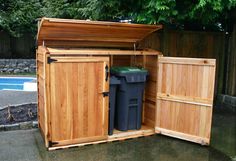 an outdoor storage shed with two trash cans and a pool in the backgroud