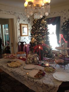 a dining room table covered in food and christmas tree with lit candles on it's side