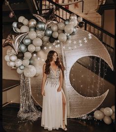 a woman in a white dress standing next to some balloons and silver stars on the wall