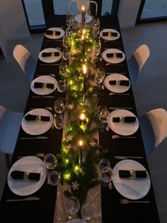 the table is set with white plates, silverware and green garlanded christmas lights