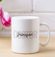 a white coffee mug with the word jameson on it next to a pink tulip