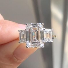 a person holding an engagement ring with three stone diamonds on it's sides and the other side