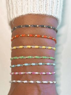 a woman's arm with several different colored bracelets on her wrist and one is wearing a white sweater