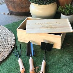 three wooden utensils sitting in a box on the ground next to potted plants