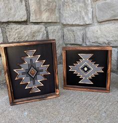 two wooden framed pictures sitting next to each other on a stone wall covered in rocks