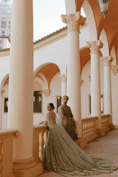 two people standing next to each other in front of some pillars and columns with arches