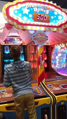 a young man standing in front of two pinball machines at an amusement park,