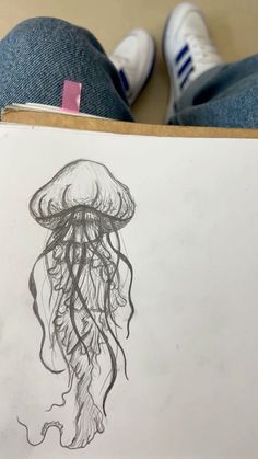 a drawing of a jellyfish on paper with someone's feet in the background